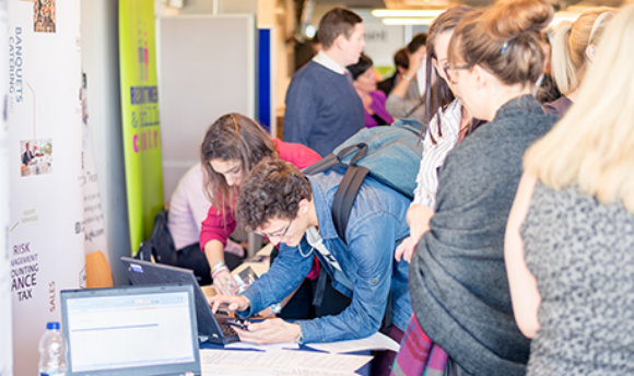 Students using a laptop at a busy recruitment fair, QMU campus, Edinburgh