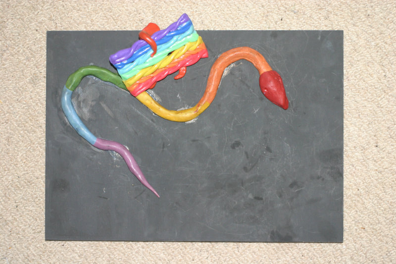A piece of rainbow clay art, a snake holding the pride flag