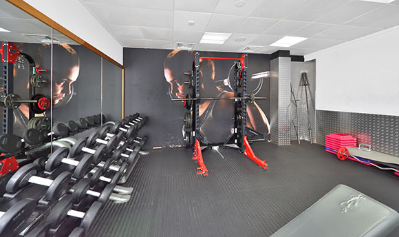 A bright, modern weights room in the gym with a large variation in weights & a squat rack