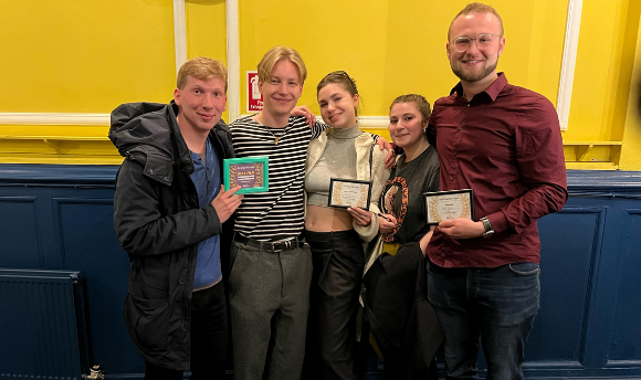 A group of students in their 20s are smiling at the camera and holding framed awards at a local film event in Edinburgh.