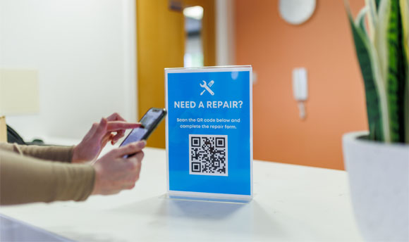 A person holding their phone up to scan a QR code for using the Accommodation repair service.