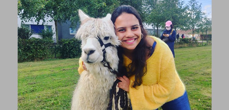 A woman in a yellow jumper smiling beside a white Llama