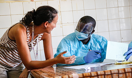 A woman leaning onto a table to talk to one of the nurses who is wearing full PPE