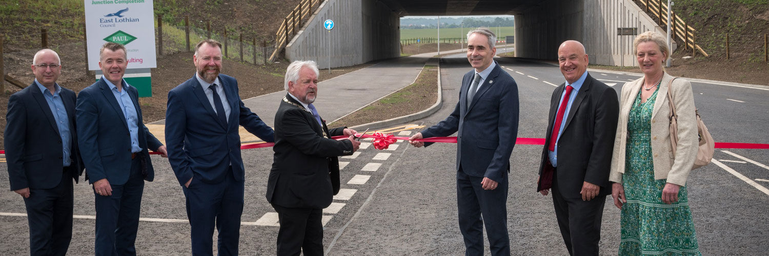 A group of people standing in line, cutting the ribbon to celebrate the opening of the new A1 junction connecting Queen Margaret University to the wider community.
