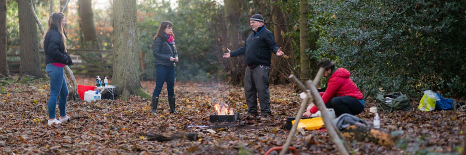 Home Economics students enjoying an outdoor learning session in a small woodland clearing, learning to carve wood and make fire.