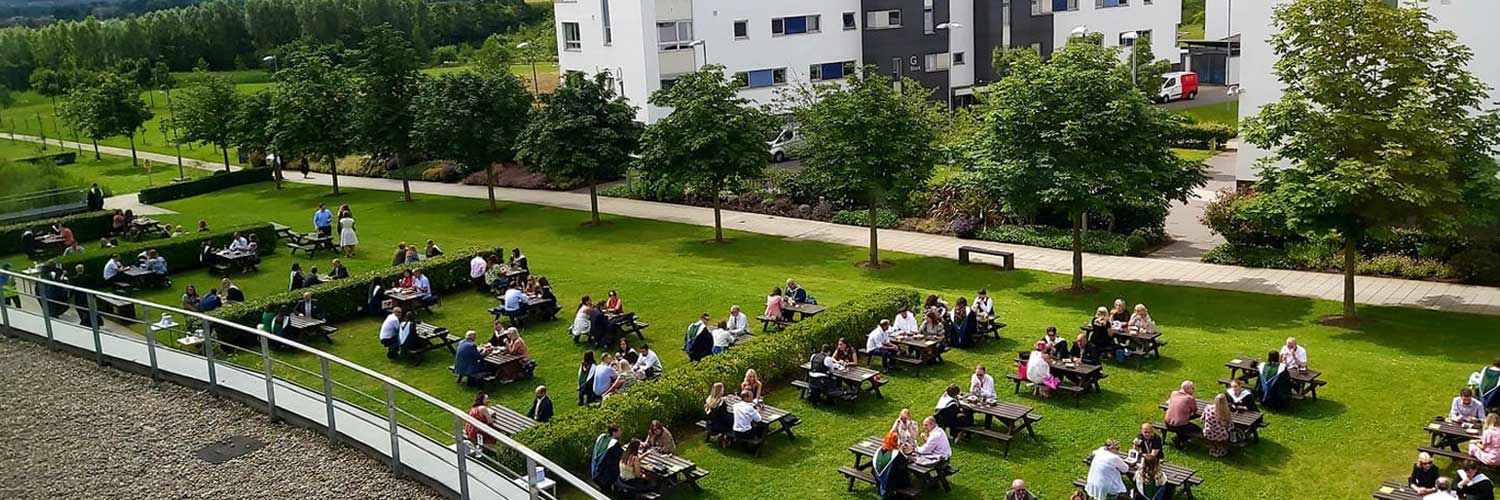 Dozens of students sitting on outdoor seating in their graduation robes.