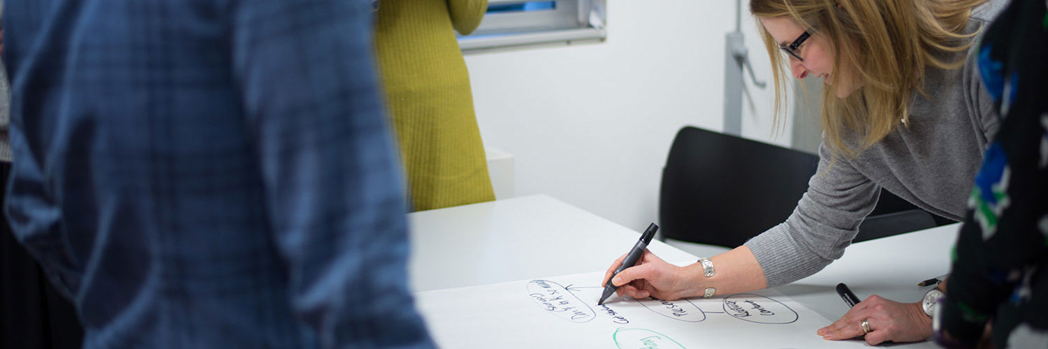 Close up of a woman writing out a mind map whilst others stand round the paper