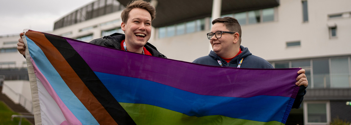 Two people holding up the LGBTQIA+ flag