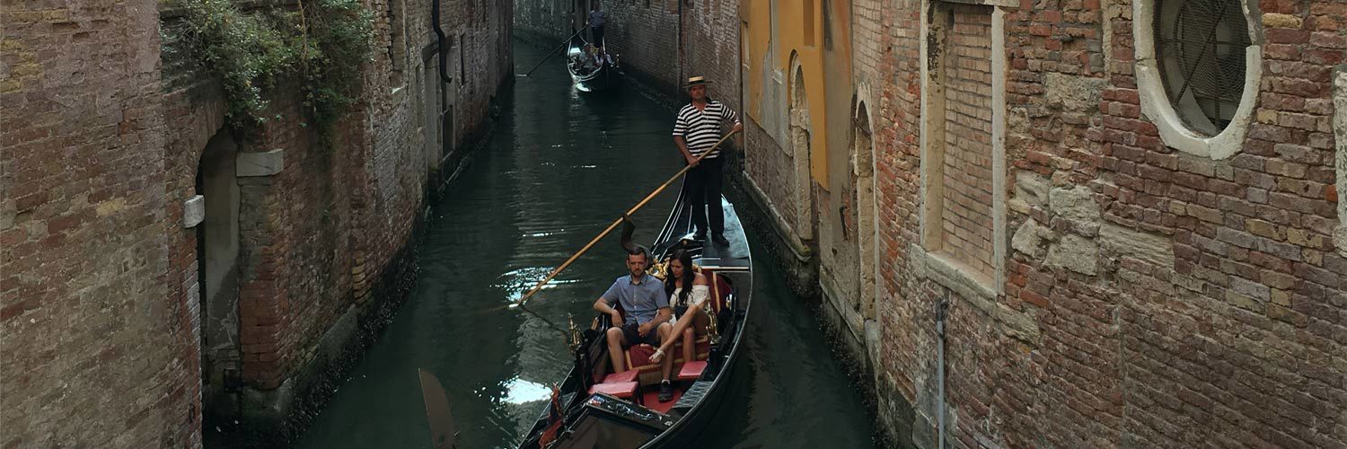 A couple riding a gondola through a building-lined canal.