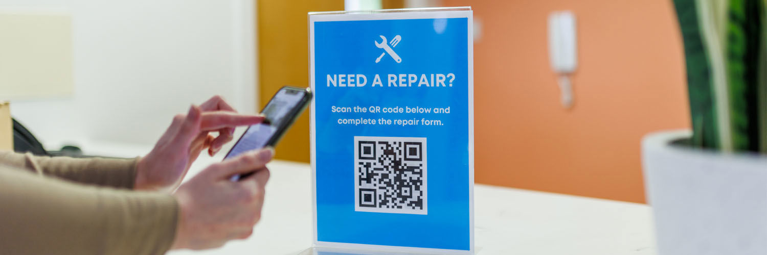 A person holding their phone up to scan a QR code for using the Accommodation repair service.