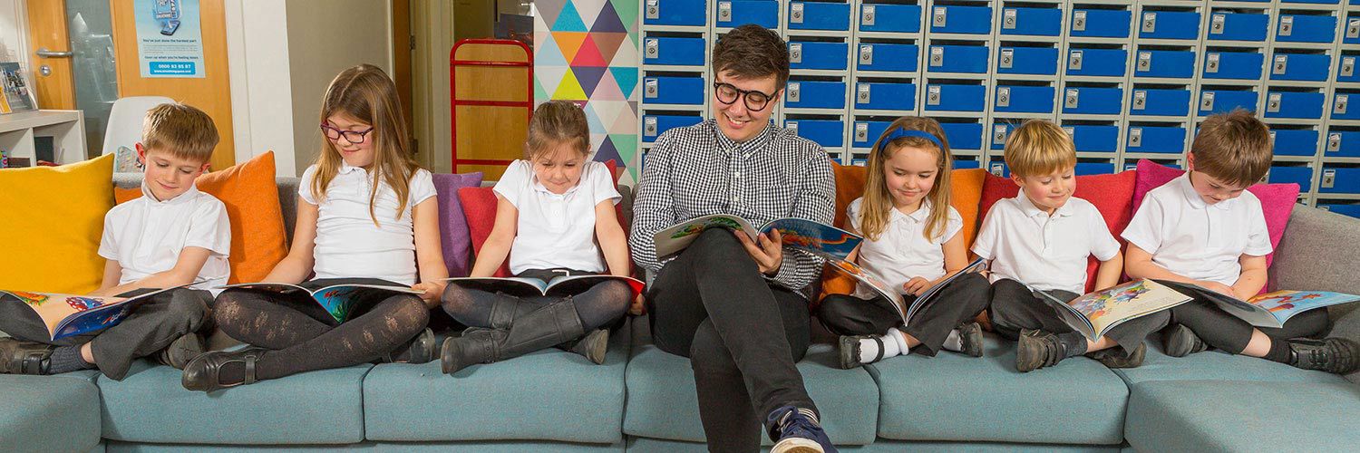 Teacher sitting on a sofa reading with some young students