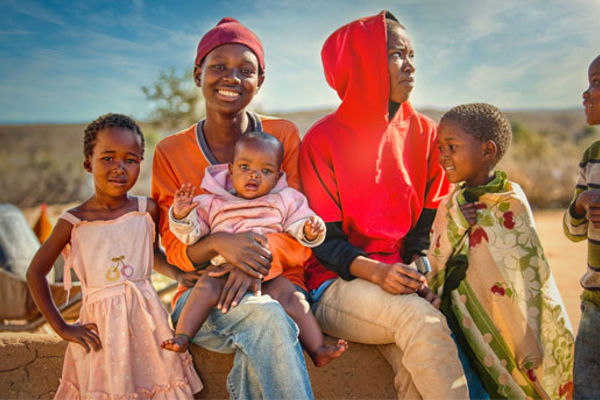 Six young people of varying ages pose for a family photo together, the youngest an infant sat on one of the older children's lap.