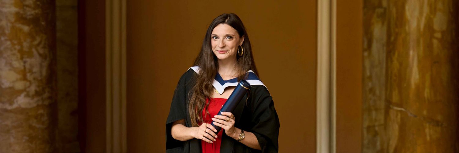 girl with long brown hair wearing graduation robe, red dress and holding a graduation scroll