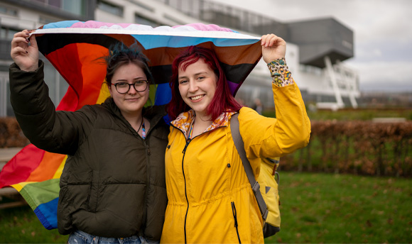 Two people holding up the LGBTQIA+ flag