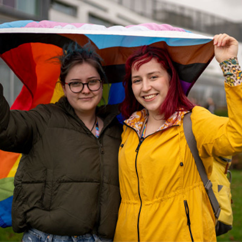 Two people holding up the LGBTQIA+ flag