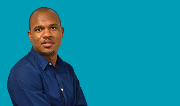 Head and shoulders shot of a Black man wearing a blue shirt and facing the camera. 
