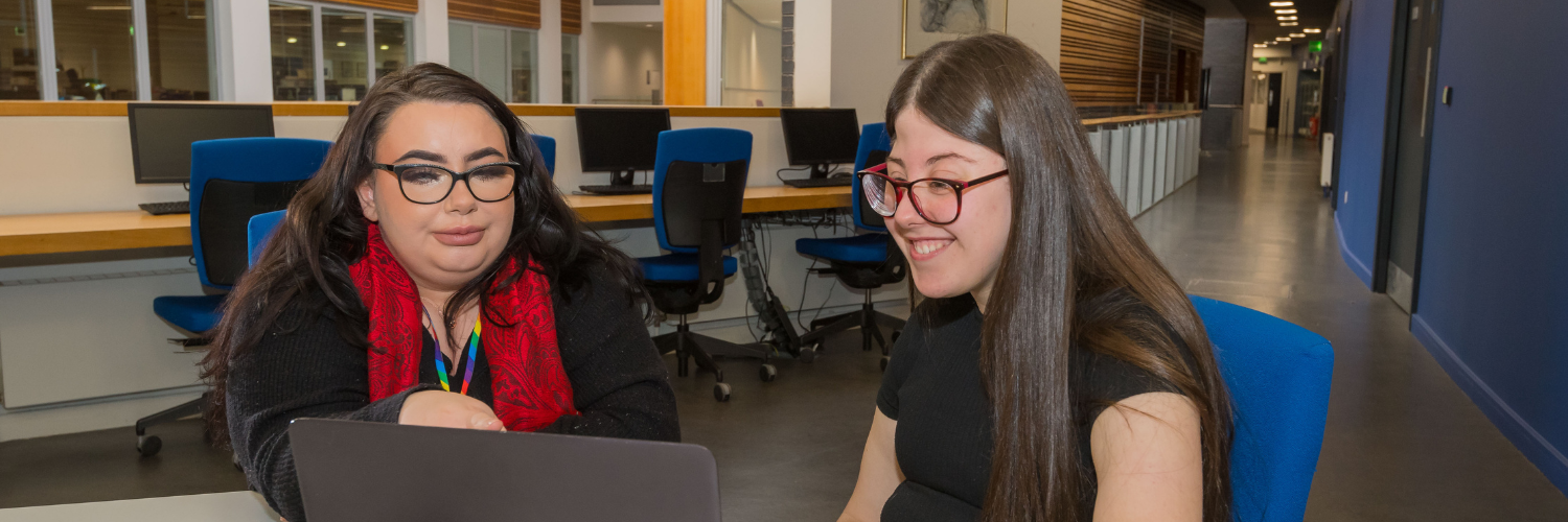 Female teacher sitting at a laptop with a female teenaged pupil