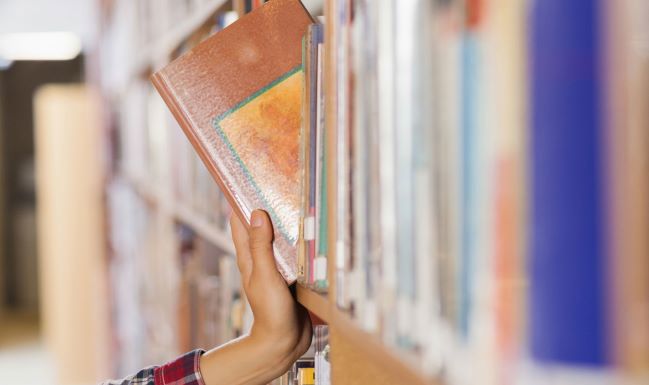Hand pulling book from library bookshelf
