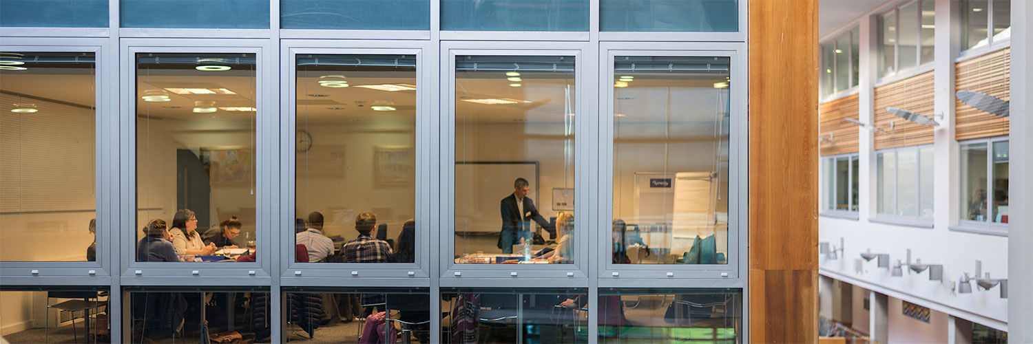 A class being taught photographed from outside through a wall of windows, QMU