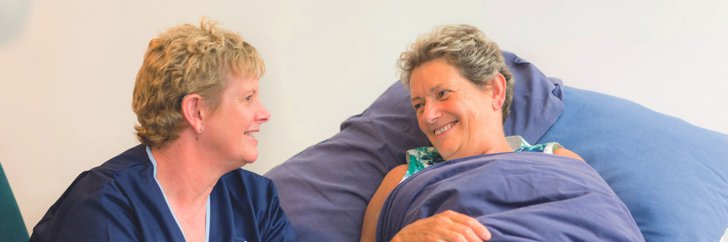 A female nurse tends to a woman lying in bed.