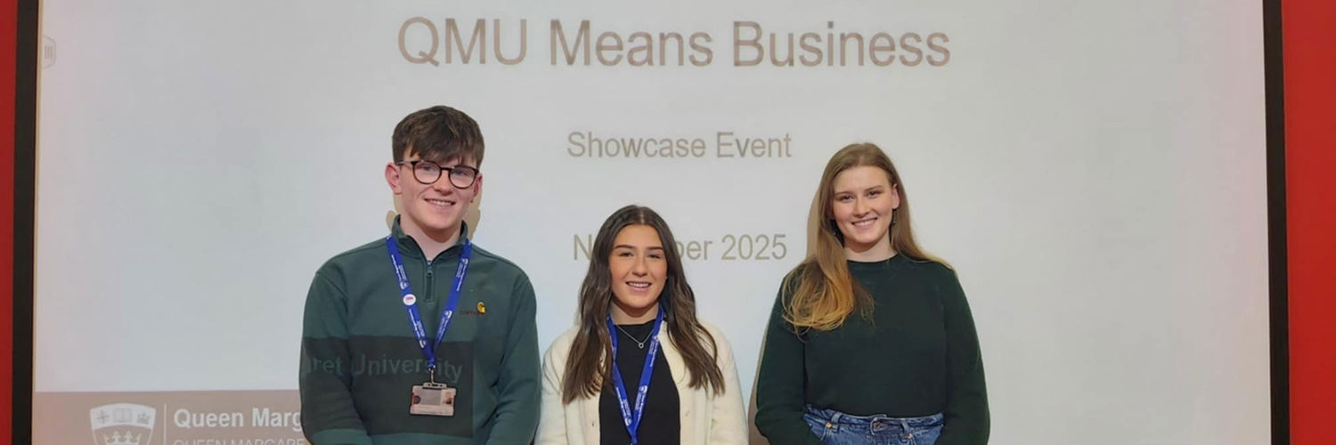 three QMU students - one young man and two young women - standing in front of a screen which says 'QMU Means Business'