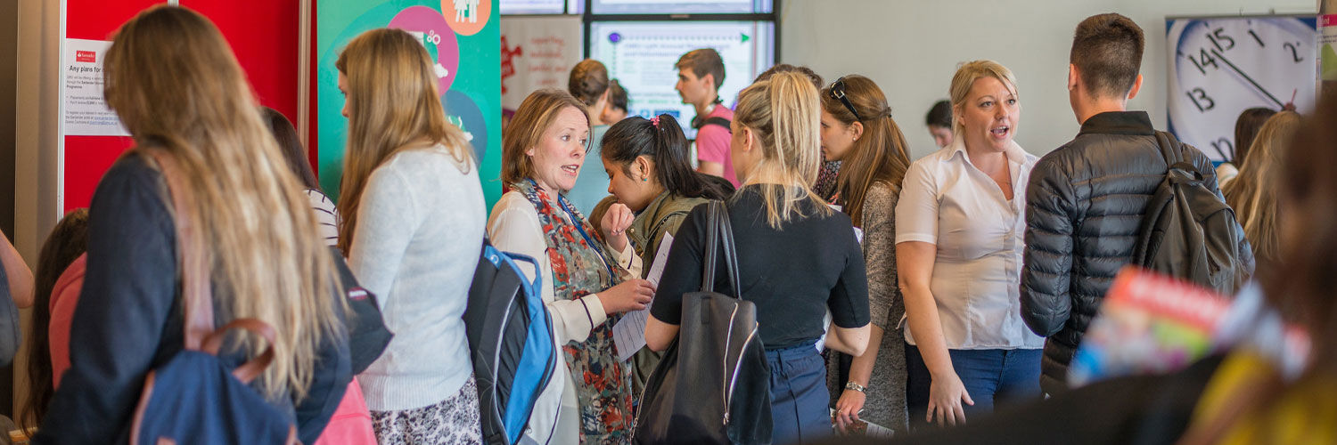 A group of people attending an event fair, in the background different stands and banners are visible.