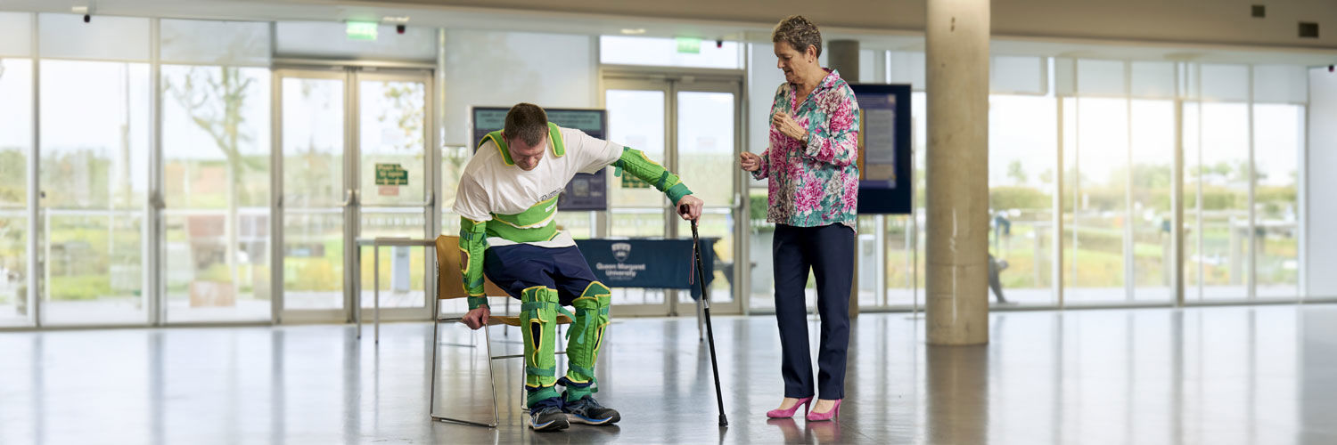 Nursing student attempts to rise from a chair while wearing an osteoporosis suite which mimics effects of the condition