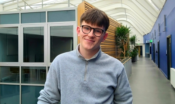 Head and shoulder shot of male student with the backdrop of the interior of Queen Margaret University