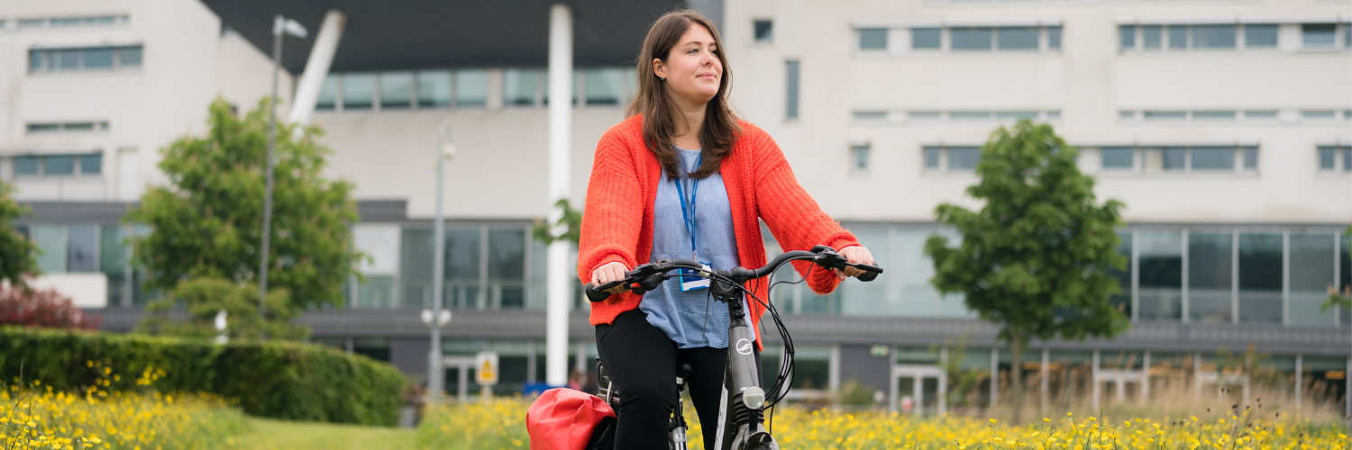 A person cycling with the Queen Margaret Unviersity campus in the background