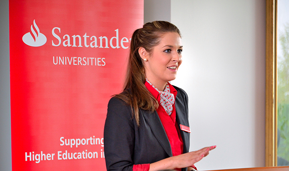 A Santander employee smiling in front of a Santander Universities sign
