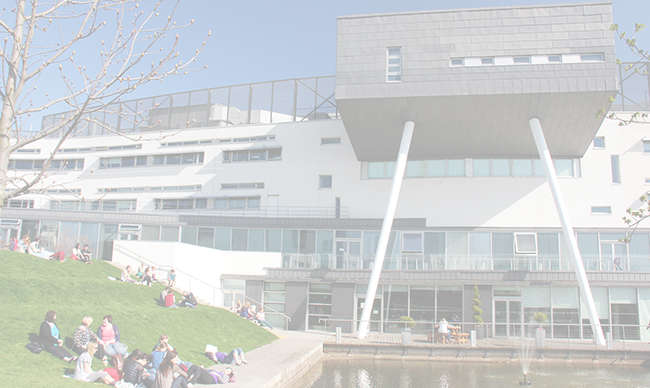 Students laying on the grass beside the fountain outside Queen Margaret University Campus