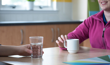 Close up of two people sat at a table, one has a glass of water and the other a mug
