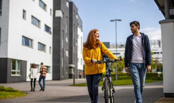 A QMU student with a bike talking to a fellow student on campus, Edinburgh