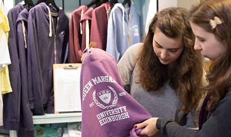 Two students holding and looking at a hoodie with the QMU logo printed on the front
