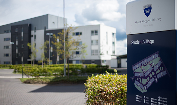 Close up of the Student Village map sign post with the building out of focus in the background