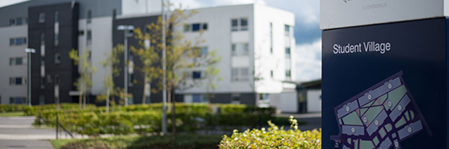 Close up of the Student Village map sign post with the building out of focus in the background