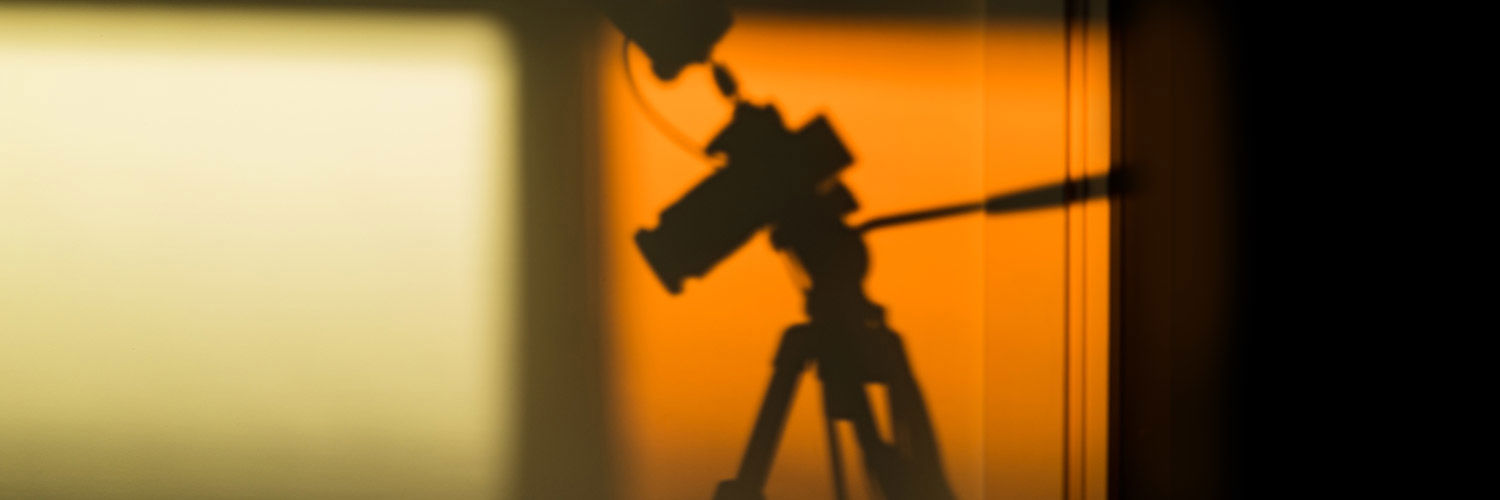 Soft silhouette of a camera on a tripod against a warm orange wall