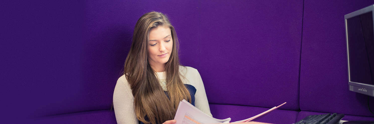 A Queen Margaret University student reading over their work against a purple wall