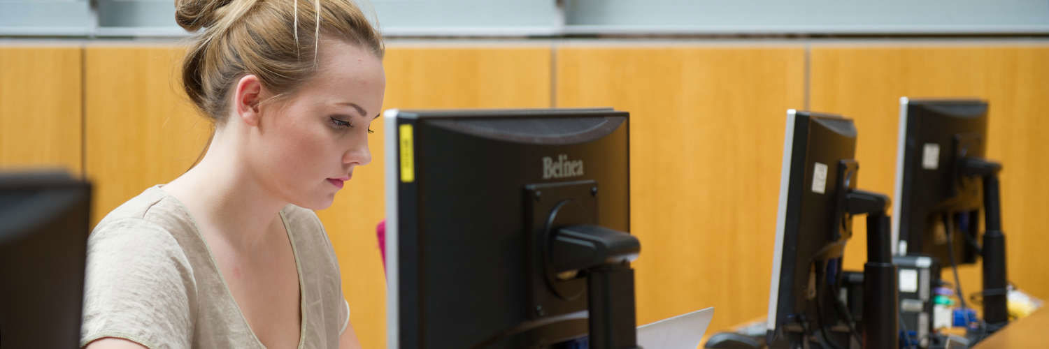 A Queen Margaret University student working alone at their computer desk, Edinburgh