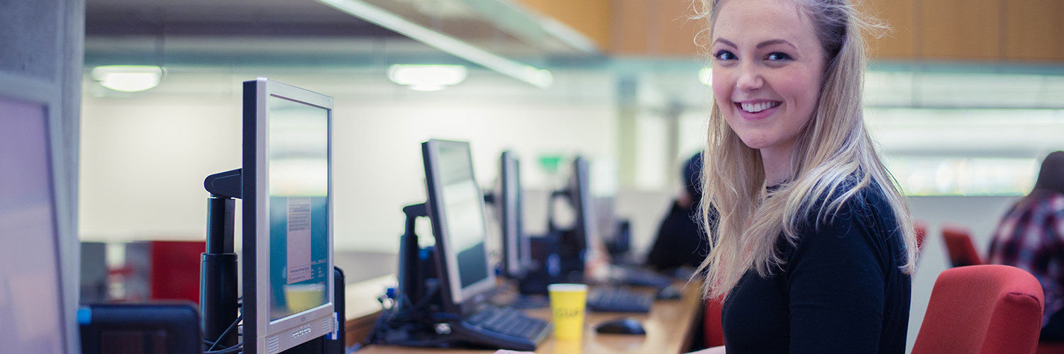 Student smiling directly at the camera whilst working on a computer, QMU, Edinburgh