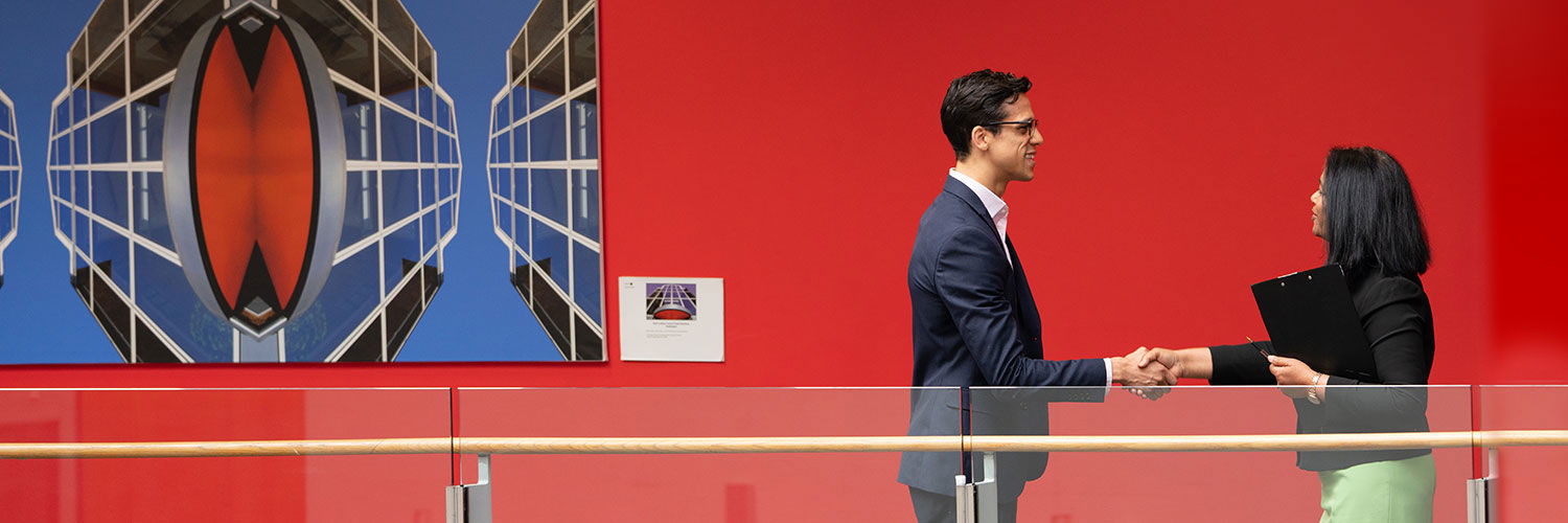Two smiling professionals shaking hands beside a large art canvas, Queen Margaret University
