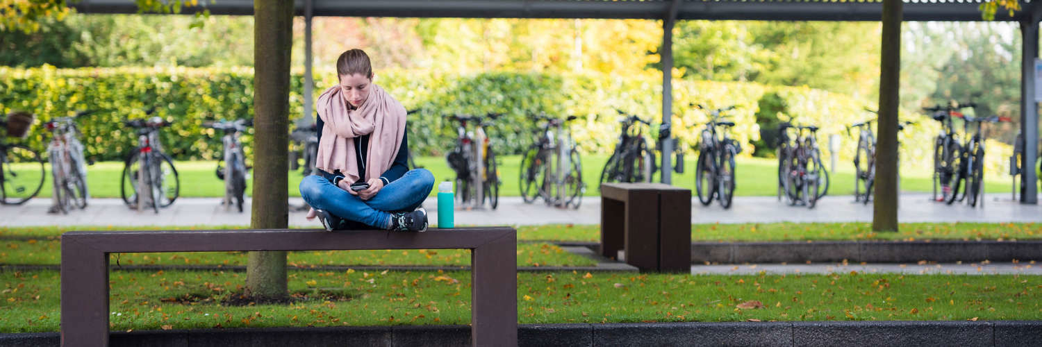 A student sitting on a sunny bench at Queen Margaret University, Edinburgh