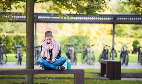 A student sitting on a sunny bench at Queen Margaret University, Edinburgh