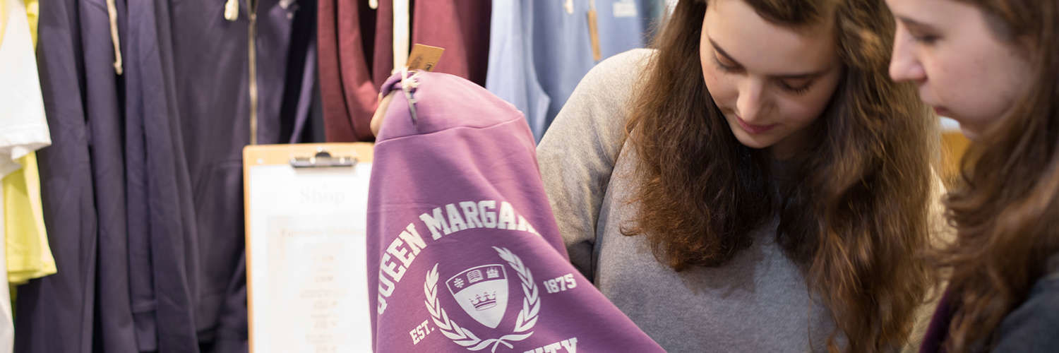 Two students holding and looking at a hoodie with the QMU logo printed on the front