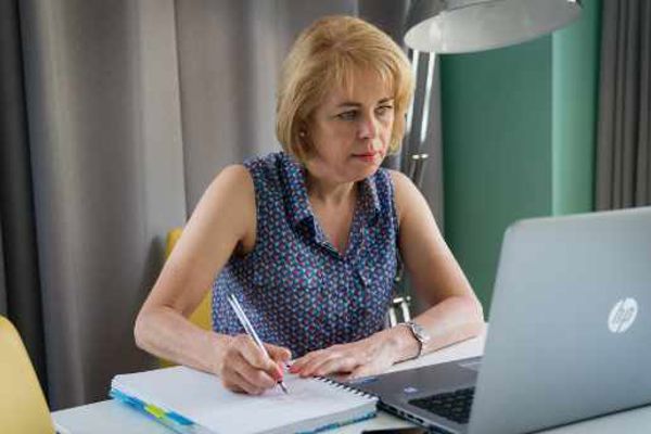 A woman sitting over a laptop and writing in a notebook