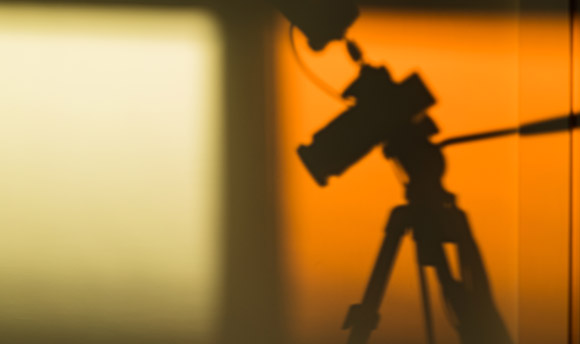 Soft silhouette of a camera on a tripod against a warm orange wall