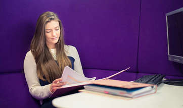 A Queen Margaret University student reading over their work against a purple wall