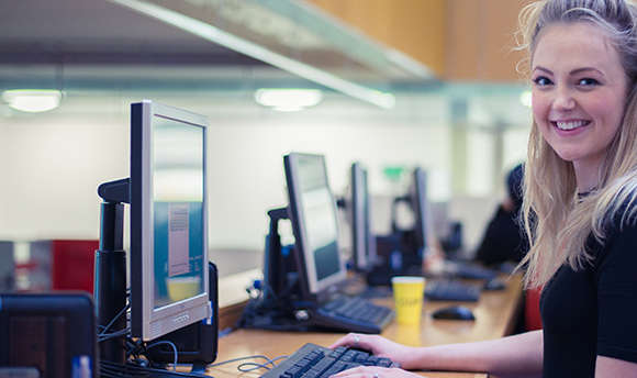 Student smiling directly at the camera whilst working on a computer, QMU, Edinburgh