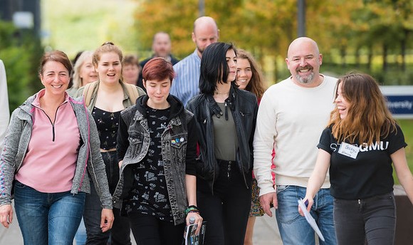 A crowd of smiling people being given a guided tour of the QMU campus on an open day