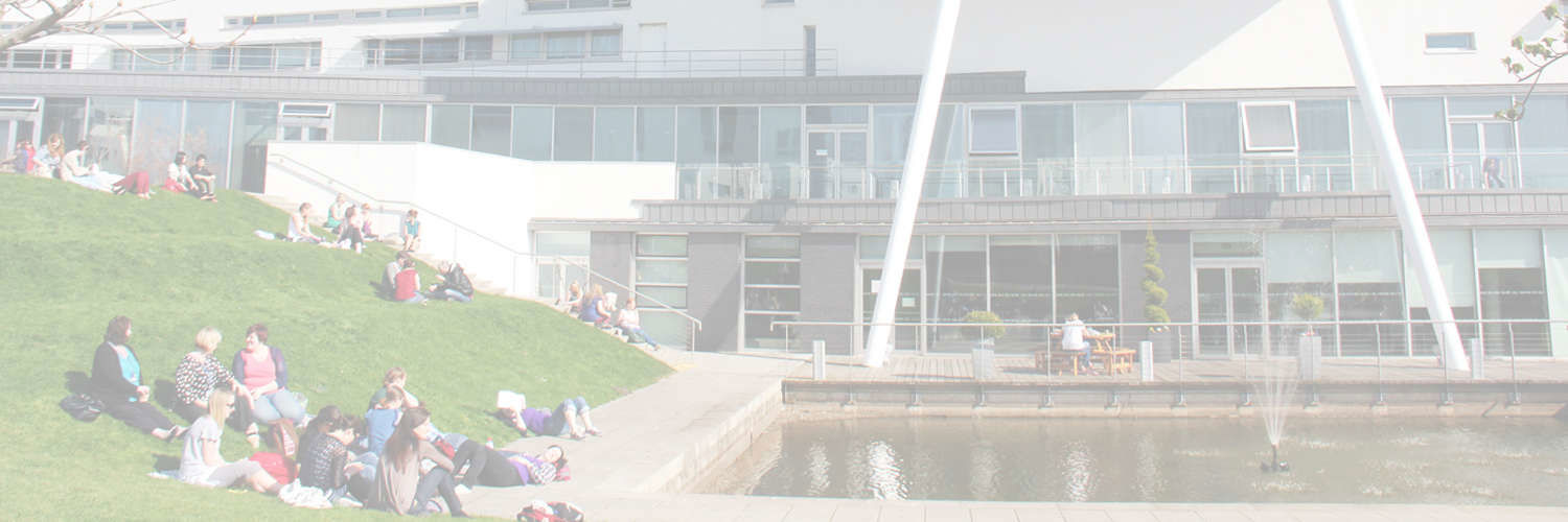 Students laying on the grass beside the fountain outside Queen Margaret University Campus